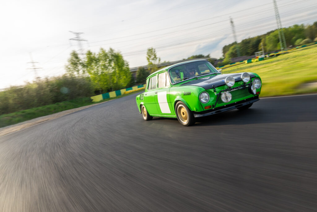Vintage green Skoda rally car racing fast on an asphalt racetrack curve with motion blur.