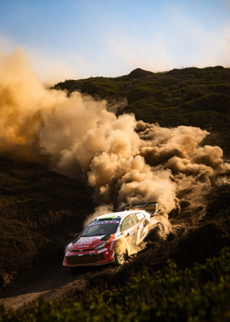 Toyota GR Yaris Rally1 car kicks up a massive dust cloud while racing on a dirt road during a WRC rally event.