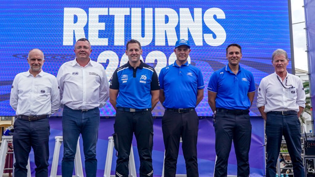 Ford motorsport and FIA officials on stage in front of a blue 'RETURNS 2026' announcement screen.