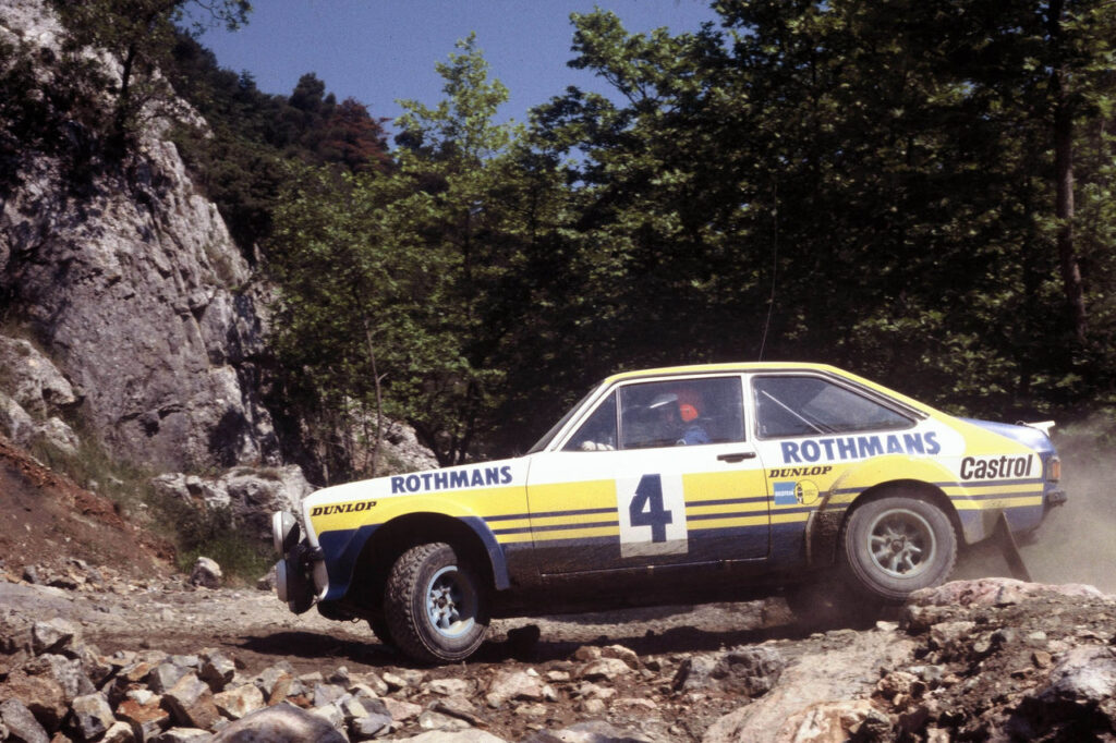 Rothmans Ford Escort MkII classic rally car racing on a rugged, rocky mountain dirt track.