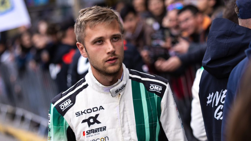 Rally driver Oliver Solberg wearing a white and green ŠKODA race suit with crowds in the background.
