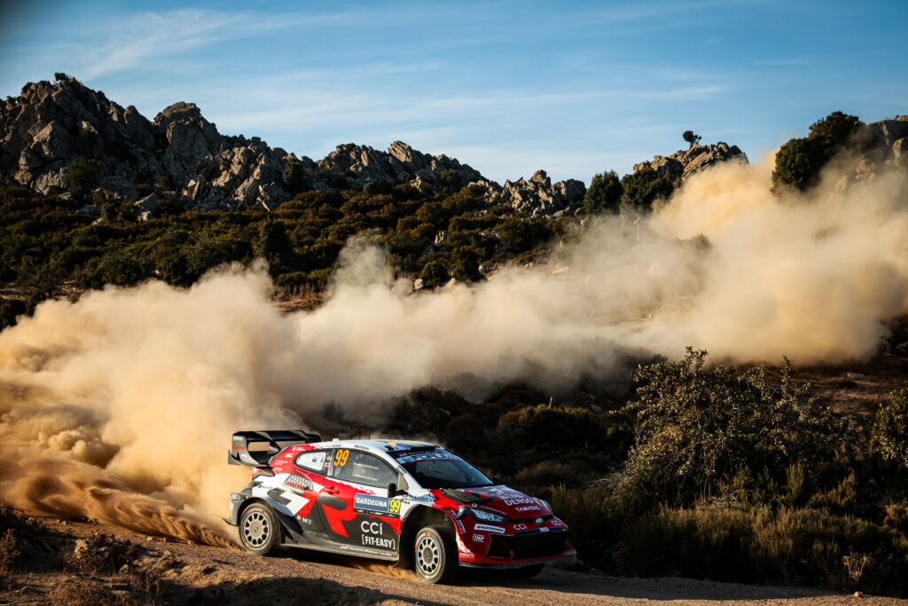 Toyota GR Yaris WRC rally car kicking up a massive dust cloud on a dirt road during Rally Italia Sardegna.